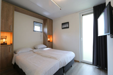 Dormitorio moderno en la cabaña Just Nature de De Wije Werelt, Países Bajos, con cama doble y televisor.