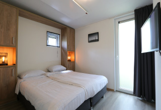 Dormitorio moderno en la cabaña Just Nature de De Wije Werelt, Países Bajos, con cama doble y televisor.