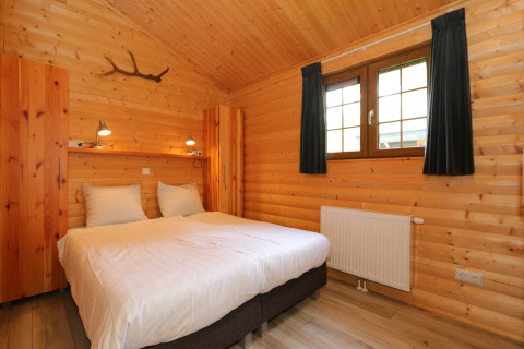 Gemütliches Schlafzimmer mit Holzverkleidung, Doppelbett, Fenster und ländlichem Flair in den Niederlanden.