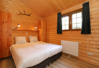 Gemütliches Schlafzimmer mit Holzverkleidung, Doppelbett, Fenster und ländlichem Flair in den Niederlanden.
