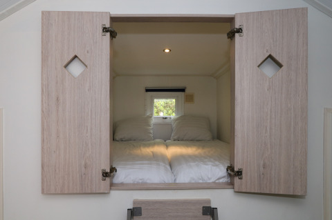 Rincón de cama con dos almohadas y puertas abiertas de madera en Forest Lodge, De Wije Werelt, Países Bajos.