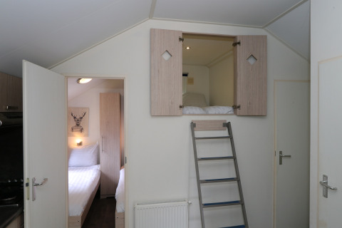 Habitación en Forest Lodge en De Wije Werelt, Países Bajos, con cama elevada y escalera visible.