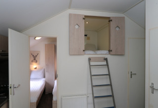 Innenraum der Forest Lodge in De Wije Werelt, Niederlande, mit Leiter und geöffnetem Schlafbereich.