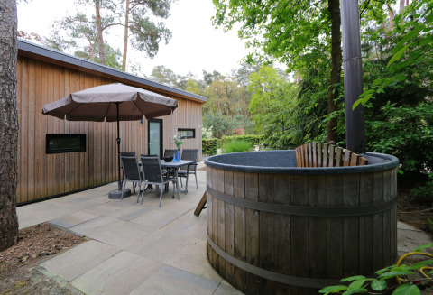 Buitenterras met houten lodge, tuinset, parasol en hottub in De Wije Werelt, Nederland.