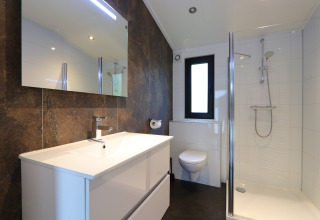 Moderne badkamer met douche, wastafel, spiegel en toilet in de Pavilion-lodge bij De Wije Werelt, Nederland.