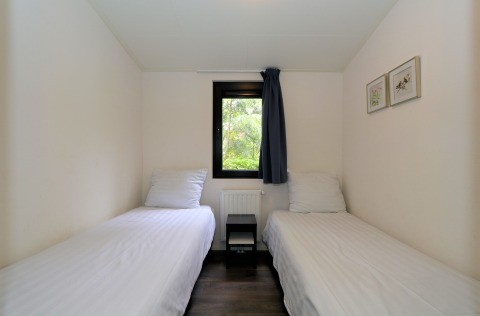 Twee eenpersoonsbedden in een compact kamertje van het Pavilion-lodge bij De Wije Werelt, Nederland, met raam.
