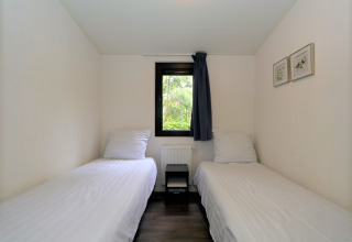 Twee eenpersoonsbedden in een compact kamertje van het Pavilion-lodge bij De Wije Werelt, Nederland, met raam.