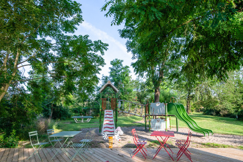 Speelplein en terras onder de bomen bij Camping Vauban, een vakantiepark in Grand Est, Frankrijk.