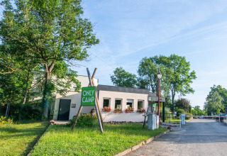 Indgang til Camping Vauban feriepark i Grand Est, Frankrig, med grønt skilt og blomster ved bygningen.