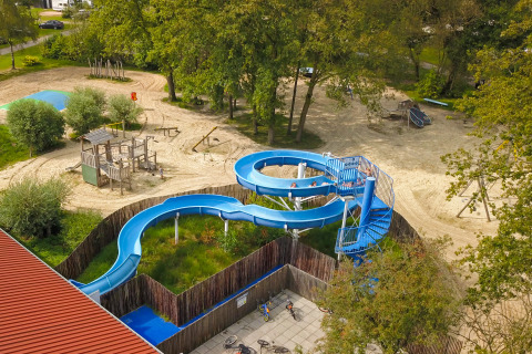 Luftaufnahme eines Spielplatzes mit blauer Rutsche und Holzklettergerüst beim Campingplatz De Rammelbeek.