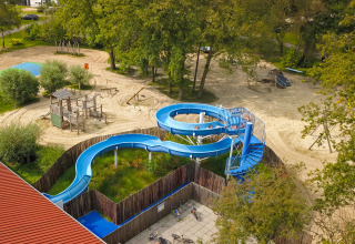 Luftaufnahme eines Spielplatzes mit blauer Rutsche und Holzklettergerüst beim Campingplatz De Rammelbeek.