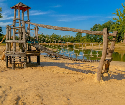 Holzspielplatz mit Hängebrücke am See auf dem Campingplatz De Rammelbeek, Overijssel, Niederlande, bei Sonne.