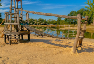 Holzspielplatz mit Hängebrücke am See auf dem Campingplatz De Rammelbeek, Overijssel, Niederlande, bei Sonne.