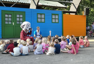 Kinder sitzen vor einer Person im Hundekostüm und einem Erwachsenen bei einer Aufführung auf einem Campingplatz.