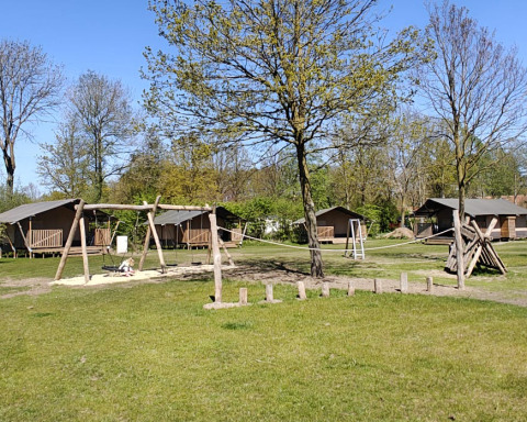Spielplatz mit Schaukeln und Holzhütten auf dem Campingplatz De Rammelbeek in Overijssel, Niederlande.