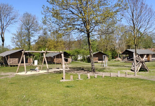 Spielplatz mit Schaukeln und Holzhütten auf dem Campingplatz De Rammelbeek in Overijssel, Niederlande.