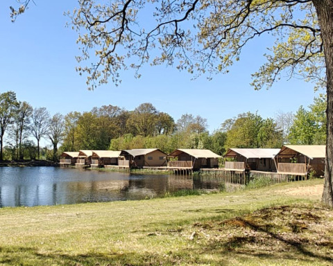 Blick auf den See und Safarizelte auf dem Campingplatz De Rammelbeek, umgeben von Bäumen in Overijssel, Niederlande.