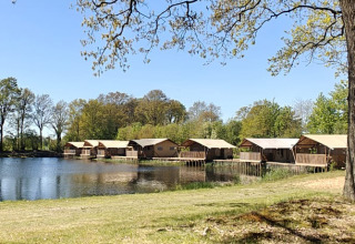 Blick auf den See und Safarizelte auf dem Campingplatz De Rammelbeek, umgeben von Bäumen in Overijssel, Niederlande.