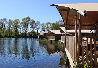 Holzhütten mit Planendach am Seeufer auf Campingplatz De Rammelbeek in Overijssel, Niederlande bei Sonnenschein.