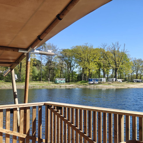 Holzterrasse am See mit Blick auf Wohnwagen und Bäume im Ferienpark De Rammelbeek, Overijssel, Niederlande.