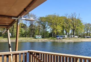 Holzterrasse am See mit Blick auf Wohnwagen und Bäume im Ferienpark De Rammelbeek, Overijssel, Niederlande.