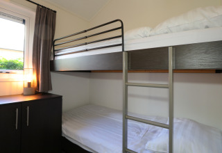 Habitación con litera, armario y lámpara en la cabaña Velthorst de De Wije Werelt, Países Bajos, luz diurna.