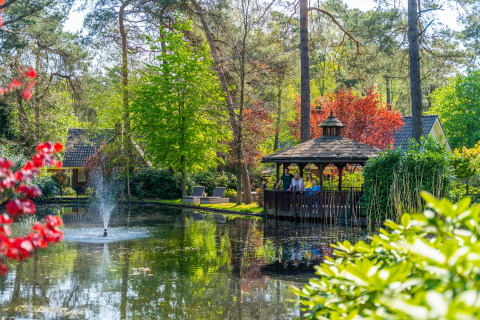 A picturesque view of a pond with fountain, gazebo, and tiny houses amid lush trees at Beekbergen, Netherlands.