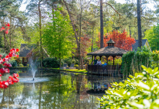 Vista pintoresca de un estanque con fuente, cenador y tiny houses entre árboles frondosos en Beekbergen.