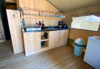 Gezellige glampingkeuken met houten kasten, gasfornuis, koffiemachines, koelkast en groot raam.