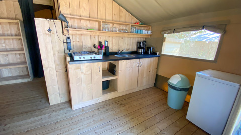 Gezellige glampingkeuken met houten kasten, gasfornuis, koffiemachines, koelkast en groot raam.