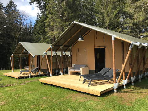 Twee safaritenten met houten terrassen en ligstoelen in een rustige, bosrijke natuuromgeving.