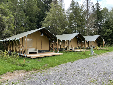 Trois tentes safari avec terrasses en bois au Camping La Sténiole en France, entourées de verdure.