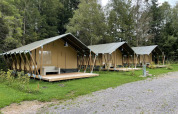 Trois tentes safari avec terrasses en bois au Camping La Sténiole en France, entourées de verdure.