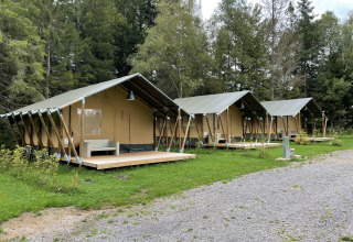 Tres tiendas safari con terrazas de madera en Camping La Sténiole, Francia, rodeadas de naturaleza.