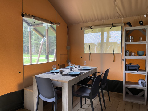Intérieur d'une tente safari au Camping La Sténiole en France, avec table à manger, chaises et étagère.