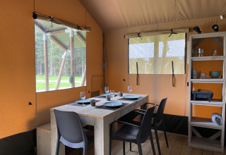 Interieur van een safaritent bij Camping La Sténiole in Frankrijk met eetafel, stoelen en rek.