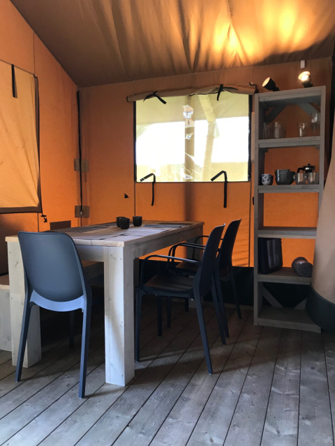 Interior of a safari tent at Camping La Sténiole in France, featuring a table, chairs, and shelves.