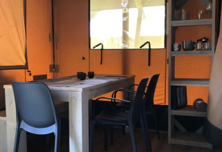 Intérieur d’une tente safari au Camping La Sténiole en France avec table, chaises et étagère.