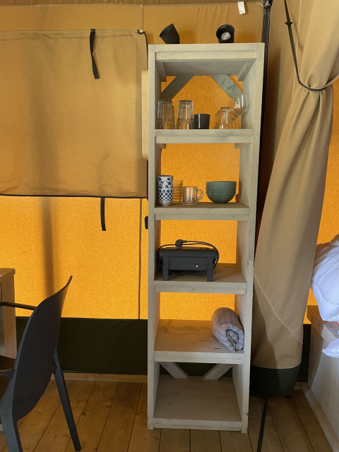 Étagère dans une tente safari au Camping La Sténiole, France, avec verres, tasses, bol et accessoires.