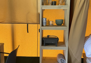Shelf in safari tent at Camping La Sténiole, France, with glasses, mugs, bowls, and other camping essentials.