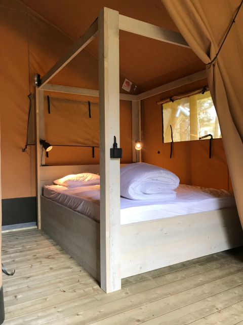 Dormitorio luminoso de tienda safari con cama doble de madera en Camping La Sténiole, Francia.