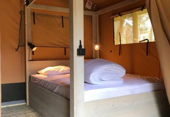 Lyst interiør af en safariteltsuite med stor dobbeltseng og trægulv på Camping La Sténiole, Frankrig.