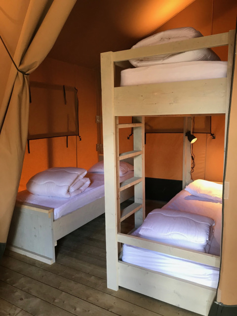 Vue intérieure d'une tente safari avec un lit superposé et un lit simple au Camping La Sténiole, France.
