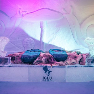 Chambre glacée à l’Iglo Lodge Burgberg, ornée de sacs de couchage, fourrures et sculptures lumineuses en glace.