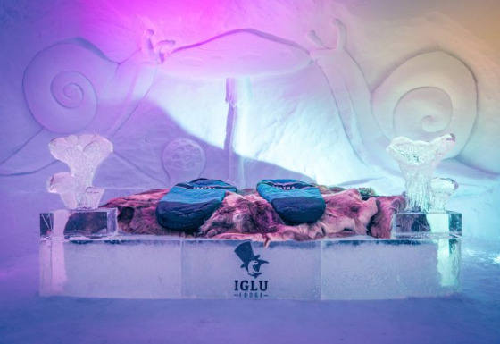 Habitación de hielo en Iglo Lodge Burgberg con sacos de dormir, pieles y esculturas de hielo iluminadas.