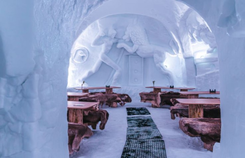 Vista interna della Iglo Lodge Burgberg con sculture di ghiaccio, tavoli in legno e panche coperte di pelliccia.