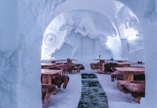Binnenzicht van Iglo Lodge Burgberg met ijssculpturen, houten tafels en met bont beklede banken.