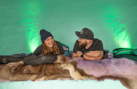 Twee personen genieten samen in een knusse iglo lodge met vachtdekens en slaapzakken.