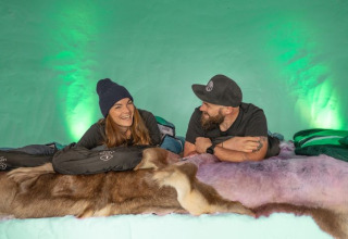 Twee personen genieten samen in een knusse iglo lodge met vachtdekens en slaapzakken.