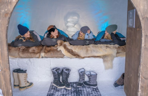Vier personen relaxen in slaapzakken op pelzen in Iglo Lodge Burgberg, omgeven door sneeuw.